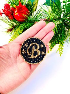 a hand holding a black and gold beaded brooch with the letter c on it