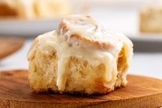 a cinnamon roll with icing sitting on top of a wooden cutting board