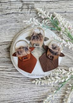 three keychains with fur on them are sitting on a white plate next to some flowers