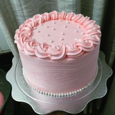 a pink frosted cake with white pearls on top sitting on a silver platter