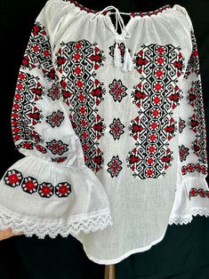 a white blouse with red and black designs on it's chest, sitting on a wooden stand