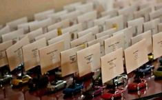 many small toy cars are lined up on the table with note cards attached to them