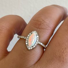 a woman's hand holding an opal and diamond ring