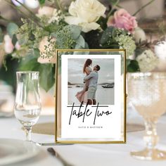 a table with flowers, wine glasses and a photo frame on it that says table two