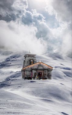 a house on top of a snowy hill with clouds in the sky over it and snow blowing behind it