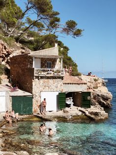 people are swimming in the water near some rocks and buildings with green shuttered doors