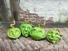 three green pumpkins with faces painted on them are sitting in front of a brick wall