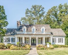 a large white house with lots of trees in the front yard and landscaping around it