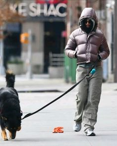 a woman walking her dog on a leash down the street while wearing a hoodie