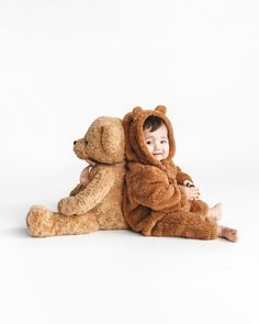 a baby sitting on the ground next to a teddy bear that is wearing a costume