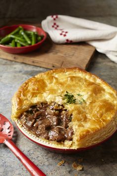 a beef pot pie on a plate with a red spatula and bowl of green beans