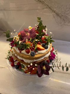 a three layer cake with berries and flowers on top