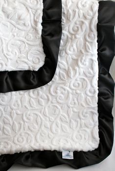 a black and white blanket with an embroidered design on the front, along with a satin ribbon