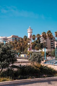 the lighthouse is surrounded by palm trees in front of some buildings and water fountains