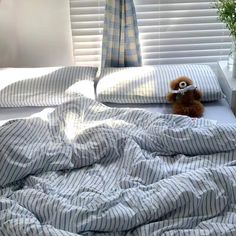 a teddy bear sitting on top of a bed in a room with striped sheets and pillows