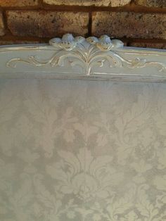 an old white bed frame with floral designs on the headboard and foot board, in front of a brick wall