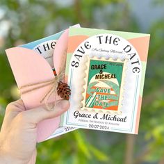 a person holding up a save the date card with a pine cone on top of it