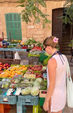 a woman standing in front of a display of fruits and vegetables at an outdoor market