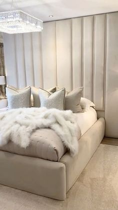 a large bed with white fur on it in a bedroom next to a chandelier