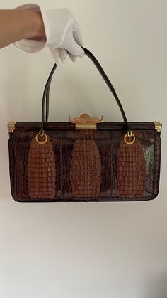 Incredibly beautiful vintage bag in crocodile look. The bag is in brown color with golden lock and details. the bag is spacious, has a large compartment in the middle and two more compartments on both sides on the outside. Interior is probably leather in beige-grey tone. Very good condition, the gold lock is a bit shabby. Dimensions: length 18.5 cm, width 34.5 cm, depth 10 cm Brown Rectangular Box Bag With Gold-tone Hardware, Formal Brown Box Bag With Gold-tone Hardware, Classic Brown Bag With Crocodile Pattern, Vintage Evening Bags With Crocodile Pattern, Vintage Crocodile Pattern Evening Bag, Brown Crocodile Pattern Satchel For Office, Brown Crocodile Pattern Top Handle Satchel, Brown Crocodile Pattern Rectangular Shoulder Bag, Elegant Vintage Brown Top Handle Shoulder Bag