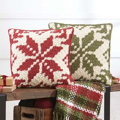 two red and green pillows sitting on top of a wooden table next to a basket