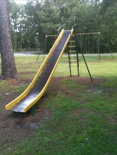 a yellow slide is in the grass next to a tree and some trees with no leaves