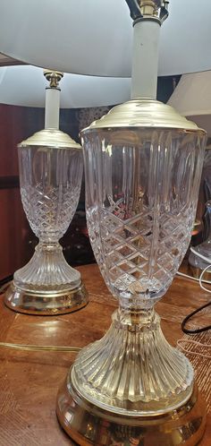 two clear glass lamps sitting on top of a wooden table next to a lamp shade