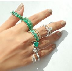 a woman's hand with several rings on it and one ring has green stones