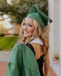 a woman wearing a green graduation gown and cap is smiling at the camera with her hands in her pockets