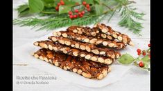 several pieces of chocolate and nuts on a white plate next to holly leaves, berries and pine cones