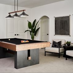 a pool table in the middle of a living room with two couches and a potted plant