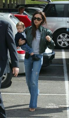 the woman is walking with her baby in her arms and she has on a leather jacket