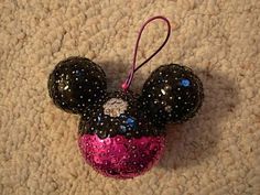 a minnie mouse ornament hanging from a string on a carpeted floor with pink and black sequins