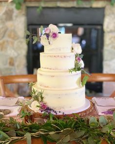 a wedding cake sitting on top of a table with greenery and flowers around it