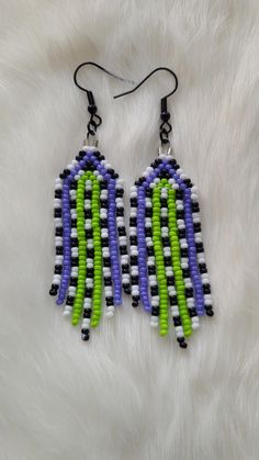 a pair of earrings with green, purple and black beads on white furnishing