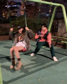 two people are sitting on swings in the park at night, one is holding onto another