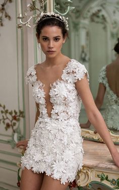 a woman in a short white dress with flowers on her head is standing next to a mirror