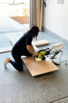 a woman in black shirt and leggings using a machine on top of a wooden table