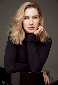 a woman sitting on top of a wooden chair with her hand on her chin and looking at the camera