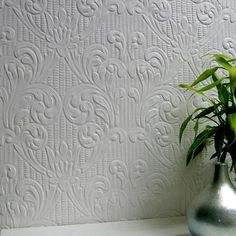 a silver vase filled with green plants on top of a white table next to a wall