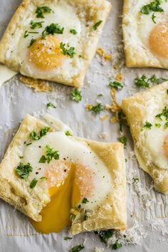 four square pastries with eggs and parsley on top, sitting on a piece of parchment paper