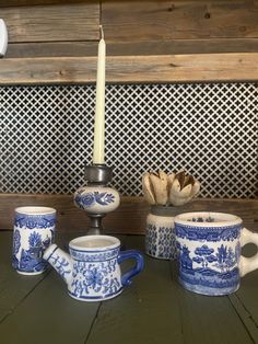 blue and white china is sitting on a table next to a lit candle, teapot, and cup