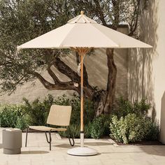 an umbrella sitting on top of a white chair next to a tree and shrubbery