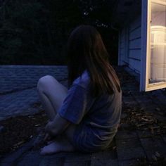 a woman sitting on the ground in front of an open refrigerator door at night time