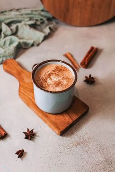 a cup of hot chocolate on a wooden board with cinnamons scattered around the table