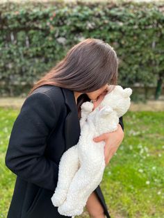 a woman holding a white teddy bear in her hands while wearing a black dress and heels