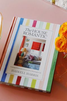 a book sitting on top of a pink table next to a vase filled with flowers