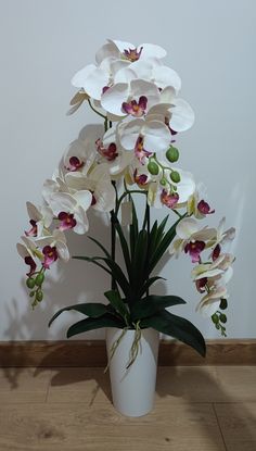 a white vase filled with lots of flowers on top of a hard wood floor next to a wall