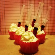 four cupcakes with white frosting and three syringes sticking out of them