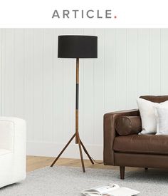 a living room with a brown leather chair and white couches in front of a wooden floor lamp